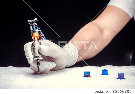 Hand of a master of the art of tattooing and a tattoo gun. Hand of a master of the art of tattooing and a tattoo gun. 85056800