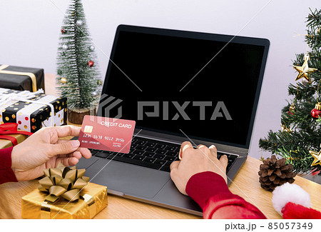 Happy woman holding credit card doing online shopping present at Christmas. Mockup laptop computer with white screen. 85057349