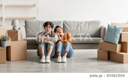 Tired Asian couple sitting on floor among carton boxes, looking at camera, feeling exhausted from moving to new home 85062004