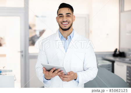 Modern Dentistry. Portrait of smiling arab dentist with digital tablet in hands Modern Dentistry. Portrait of smiling arab dentist with digital tablet in hands 85062125