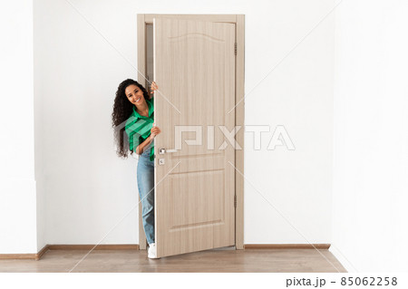 Cheerful lady looking out of door standing in doorway Cheerful lady looking out of door standing in doorway 85062258