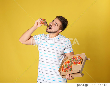 Handsome man eating tasty pizza on yellow background 85063618