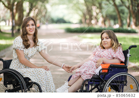 Smiling women in wheelchairs holding hands at park 85065632