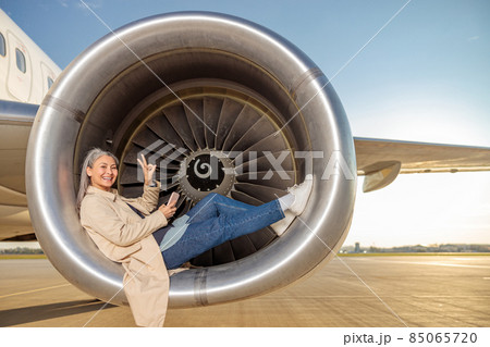 Joyful woman with smartphone lying in aircraft engine Joyful woman with smartphone lying in aircraft engine 85065720