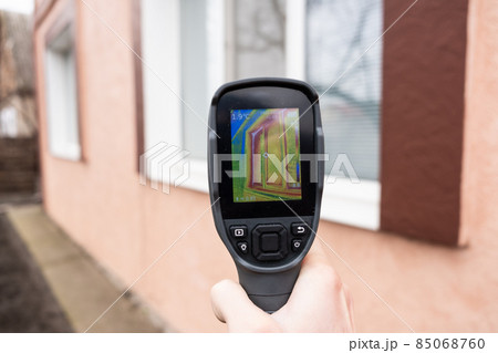 A male hand holds a thermal imager at the window of a house. Search for heat loss in private houses. A male hand holds a thermal imager at the window of a house. Search for heat loss in private houses. 85068760