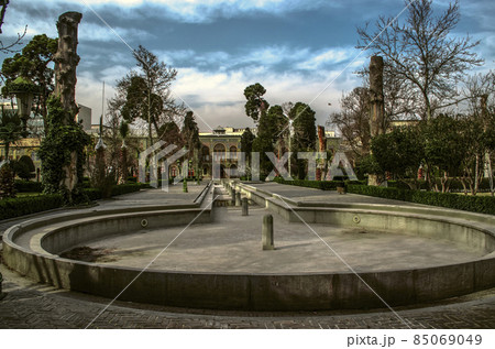 An oval pool with a long ditch and 12 fountains next to a paved path through an old winter garden near the Palace of the Sun in Tehran. 85069049