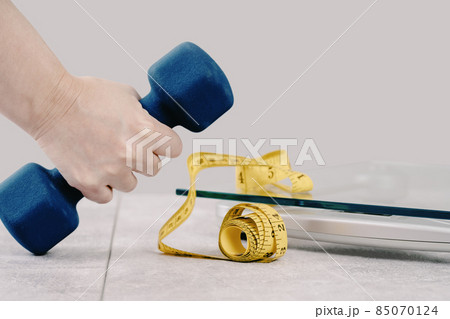 Hand with a dumbbell and measuring tape on gray background 85070124