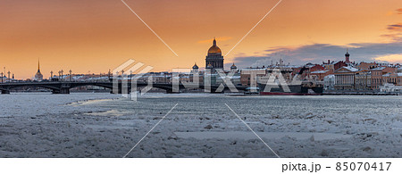 Winter panoramic view of St. Petersburg at sunset, Isaac cathedral and Blagoveshenskiy bridge on background, steam over frozen Neva river, huge ship moored near embankment, sky of orange color Winter panoramic view of St. Petersburg at sunset, Isaac cathedral and Blagoveshenskiy bridge on background, steam over frozen Neva river, huge ship moored near embankment, sky of orange color 85070417