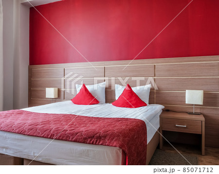 Large double bed with pillows with a wooden headboard against the background of a red wall. Place for text 85071712