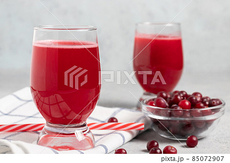 Two glasses with homemade freshly cranberry juice and a bowl of cranberries on a gray concrete table 85072907