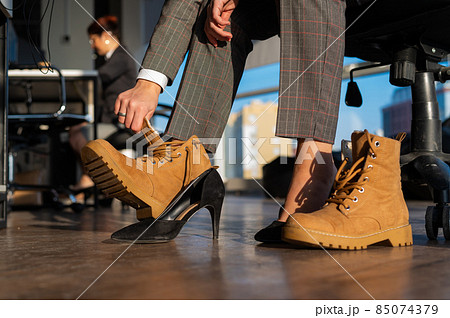 Business woman changes shoes with high heels on boots in the office. End of the working day. Tired legs Business woman changes shoes with high heels on boots in the office. End of the working day. Tired legs 85074379