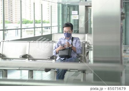 Man commuter with face mask on sitting on waiting lounge for transport. Masked transit concept. Man commuter with face mask on sitting on waiting lounge for transport. Masked transit concept. 85075679