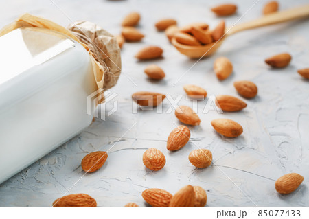Milk from organic almonds in a transparent bottle with a scattering of seeds and a wooden spoon on a light background Milk from organic almonds in a transparent bottle with a scattering of seeds and a wooden spoon on a light background 85077433