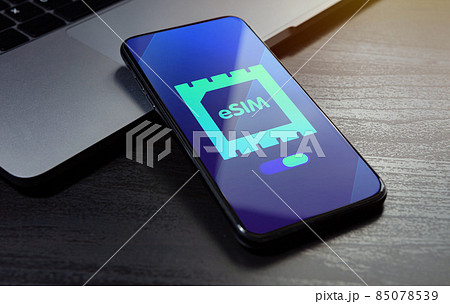 eSIM technology concept. Embedded SIM electronic phone sim card - mobile cellular global internet communication technology. Close up smartphone lying on a wooden table with an esim icon on the screen 85078539