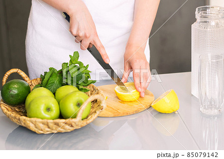 Woman making detox drink with lemon and mint in the kitchen at home. Rejuvenating invigorating water lemon, antioxidant. 85079142