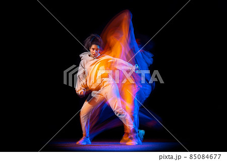 Sportive young girl in white costume dancing hip-hop dance isolated on dark background at dance hall in neon mixed light. Sportive young girl in white costume dancing hip-hop dance isolated on dark background at dance hall in neon mixed light. 85084677