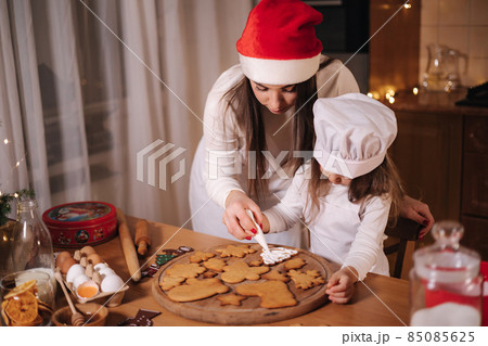 Mom in santas hat with her little doughter decorates gingerbread using glaze. Christmas and New Year traditions concept. Christmas bakery. Happy holidays Mom in santas hat with her little doughter decorates gingerbread using glaze. Christmas and New Year traditions concept. Christmas bakery. Happy holidays 85085625