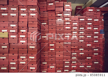Big wall of lots of red cardboard package boxes with footwear stacked at a factory warehouse. Shoe manufacturing industry, bulk trade, distribution and business concepts 85085911