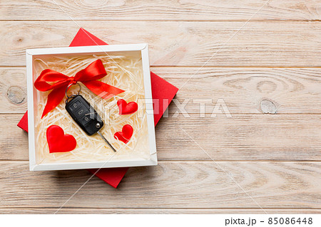Black car key in a present box with a ribbon and red heart on colored background. Valentine day composition Top view 85086448