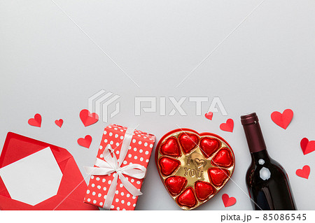 Bottle of red wine on colored background for Valentine Day with gift box, envelope and chocolate. Heart shaped with gift box of chocolates top view with copy space Bottle of red wine on colored background for Valentine Day with gift box, envelope and chocolate. Heart shaped with gift box of chocolates top view with copy space 85086545