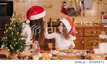 Process of mom and daughter baking at home. Raw dough for cooking Christmas cookies gingerbread on wooden table. Candle light at evening time. Fir tree Process of mom and daughter baking at home. Raw dough for cooking Christmas cookies gingerbread on wooden table. Candle light at evening time. Fir tree 85086872