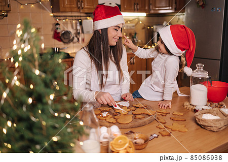 Mom with adorable little daughter spend time at kitchen in Christmas eve. Girls preparing sweets for holidays. Gingerbread and candy. Happy family Mom with adorable little daughter spend time at kitchen in Christmas eve. Girls preparing sweets for holidays. Gingerbread and candy. Happy family 85086938