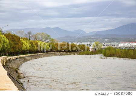 Beautiful daylight scenery of snowy Caucasus mountains with a wavy lake in front and modern buildings in the middle 85087080