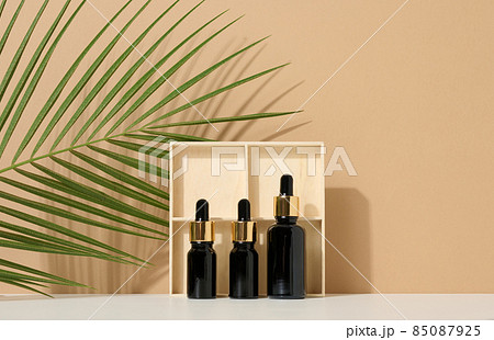 glass brown bottle with pipette on light brown background, near palm leaf. Mockup skincare cosmetic product glass brown bottle with pipette on light brown background, near palm leaf. Mockup skincare cosmetic product 85087925