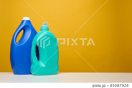 plasticd blue large bottles with liquid detergent stand on a white table, yellow background plasticd blue large bottles with liquid detergent stand on a white table, yellow background 85087926