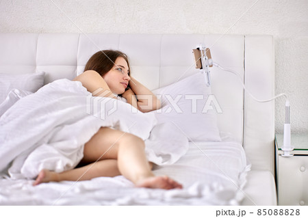 Home holder for phone with clip is attached above bed of woman who is watching movie. Home holder for phone with clip is attached above bed of woman who is watching movie. 85088828