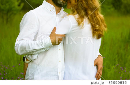 Newlyweds. Beautiful couple in love gently embracing standing in a green meadow in summer. Husband and wife in white shirts showing their feelings for each other. Devotion, purity, harmony, love theme Newlyweds. Beautiful couple in love gently embracing standing in a green meadow in summer. Husband and wife in white shirts showing their feelings for each other. Devotion, purity, harmony, love theme 85090656