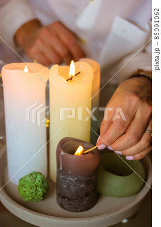 Woman lighting fire on white and green soy, wax scented candles, holding burning match in hand. Cozy home. Romantic mood, preparing for date. Christmas evening, New Year 2022 vertical photo. Spa time. 85091062