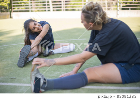 Happy young female friends warming up on football field Happy young female friends warming up on football field 85091235