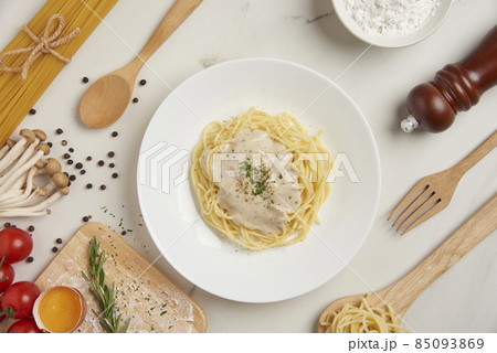 pasta concept a dish of boiled long slim pasta being served on the white tile table together with a wooden spoon and fork, tiny red tomato, and other ingredients 85093869