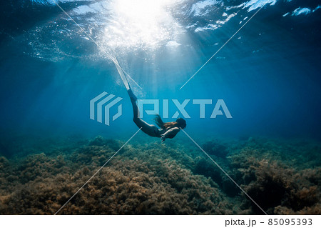 Freediver woman with fins glides underwater in tropical blue. Freediver woman with fins glides underwater in tropical blue. 85095393