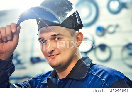 Portrait of Metal Locksmith. Young Caucasian man looks into camera from under visor of protective Portrait of Metal Locksmith. Young Caucasian man looks into camera from under visor of protective 85096691