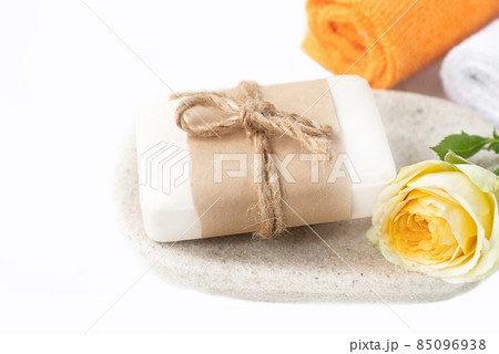 Piece of organic soap wrapped in craft paper on tray with fresh yellow rose and colorful rolled towels on bathroom table Piece of organic soap wrapped in craft paper on tray with fresh yellow rose and colorful rolled towels on bathroom table 85096938