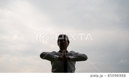 Young businessman meditating under grey sky 85096988