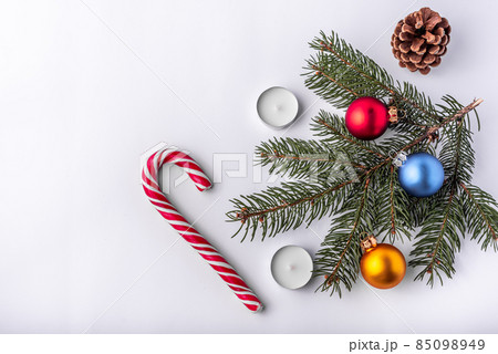 Christmas and new year flat lay: green fir branch, cone, red, blue and yellow balls, two candles and caramel candy on white isolated background. 85098949