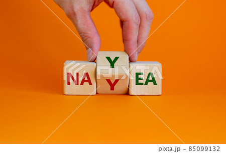 Yea or nay symbol. Businessman turns a cube, changes the word 'nay' to 'yea'. Beautiful orange background. Copy space. Business, motivation and yea or nay concept. 85099132