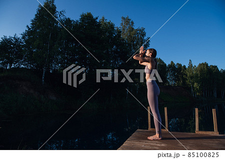 Beautiful young woman performing a spiritual yoga pose on a forest lake at sunny day, sunrise zen wellness Beautiful young woman performing a spiritual yoga pose on a forest lake at sunny day, sunrise zen wellness 85100825