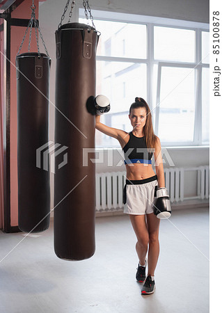 Female kickboxer hitting punching bag while dust particles flies in sunflare light background. Female kickboxer hitting punching bag while dust particles flies in sunflare light background. 85100878