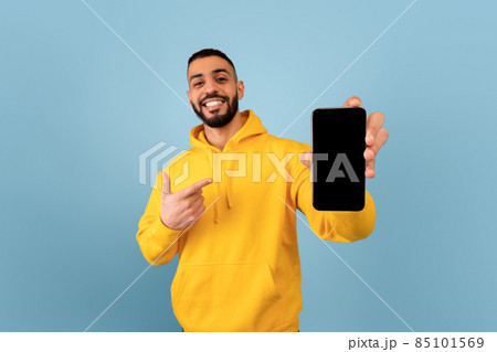 Cellphone with blank screen in arab man hand, happy guy pointing at brand new mobile phone, blue background Cellphone with blank screen in arab man hand, happy guy pointing at brand new mobile phone, blue background 85101569