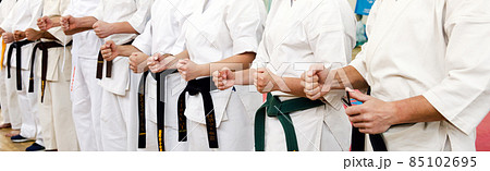 Karate master in a white kimono and with a black belt, stands in front of the formation of his students. Martial arts school in training in the gym. 85102695