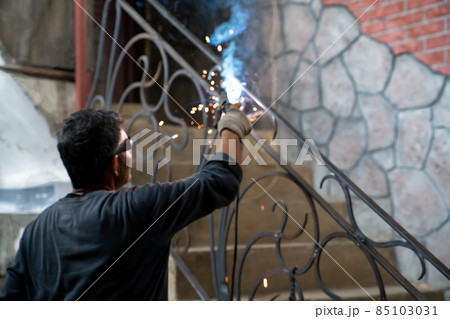 Man in safety glasses is welding metal of staircase. Welding work on metal in private house. blurred background. 85103031