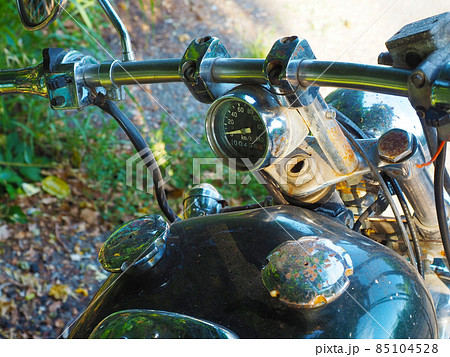 Fragment of a motorcycle with a rusting handlebar and speedometer on it and rust-covered caps on the gas tank 85104528