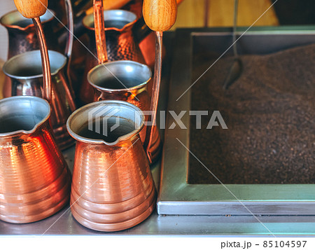 Shiny bronze-colored metal turks stand next to sand to make oriental coffee 85104597