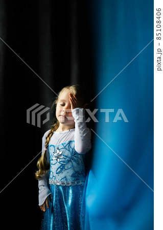 Portrait of a little girl on a dark blue background. Fatigue, the child is holding on to his head. Front view. 85108406