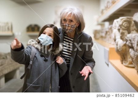 Senior woman and preteen girl in protective masks viewing ancient sculptures in museum Senior woman and preteen girl in protective masks viewing ancient sculptures in museum 85109462