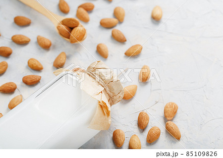Milk from organic almonds in a transparent bottle with a scattering of seeds and a wooden spoon on a light background 85109826